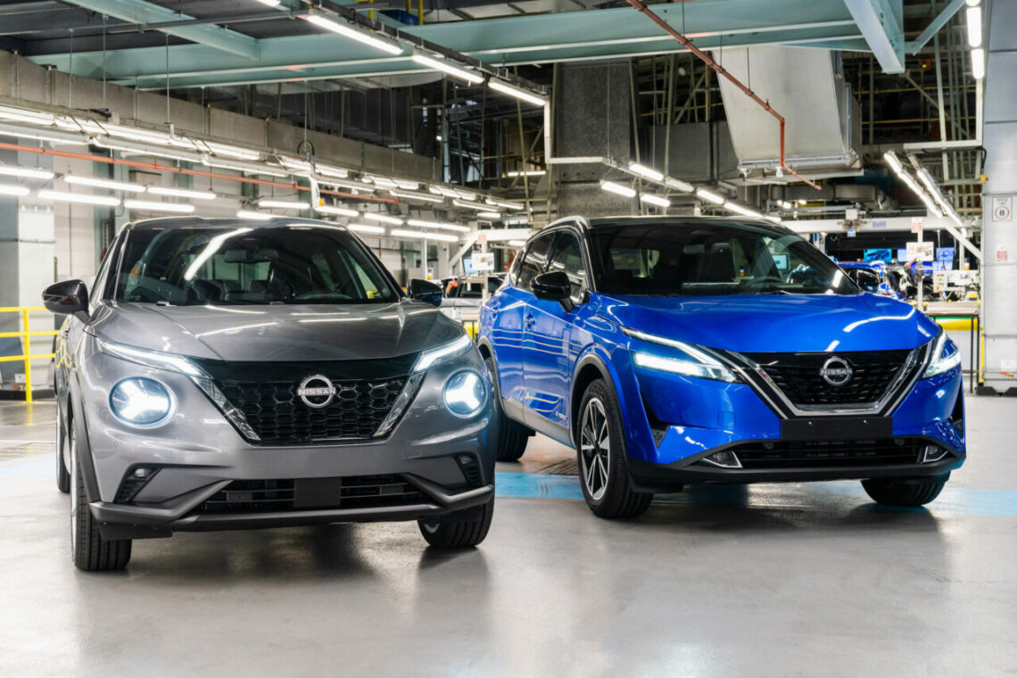 Dois carros elétricos Nissan.  Um cinza, o outro azul, estão na fábrica da empresa japonesa, prontos para funcionar.