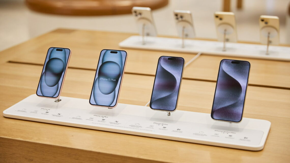 Quatro smartphones alinhados em exposição numa loja, com etiquetas de modelo e especificações na parte inferior.